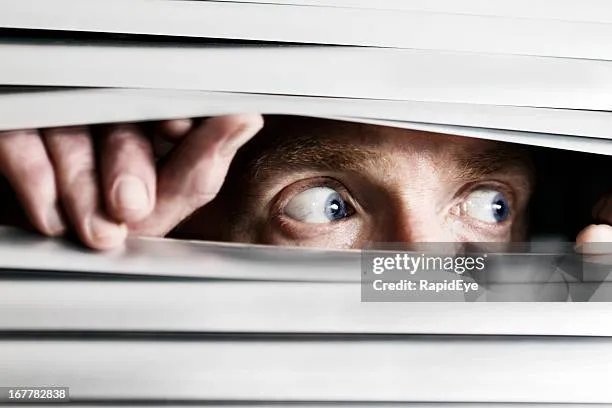 Paranoid man looking through blinds