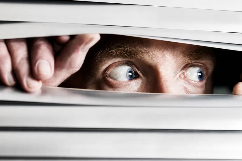 Paranoid man looking through blinds